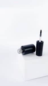 Nail polish bottle and brush applicator on a plain white surface
