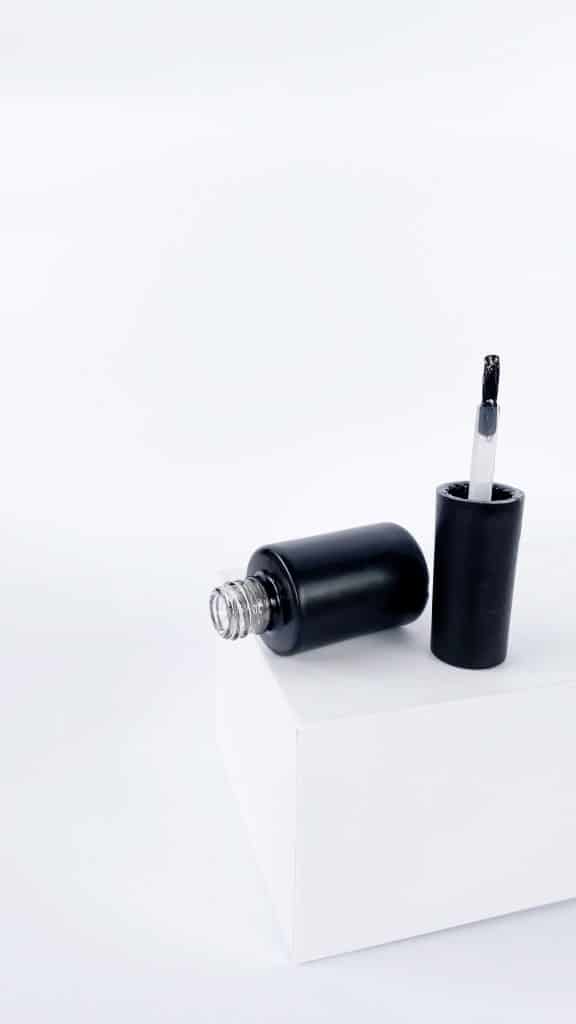 Nail polish bottle and brush applicator on a plain white surface