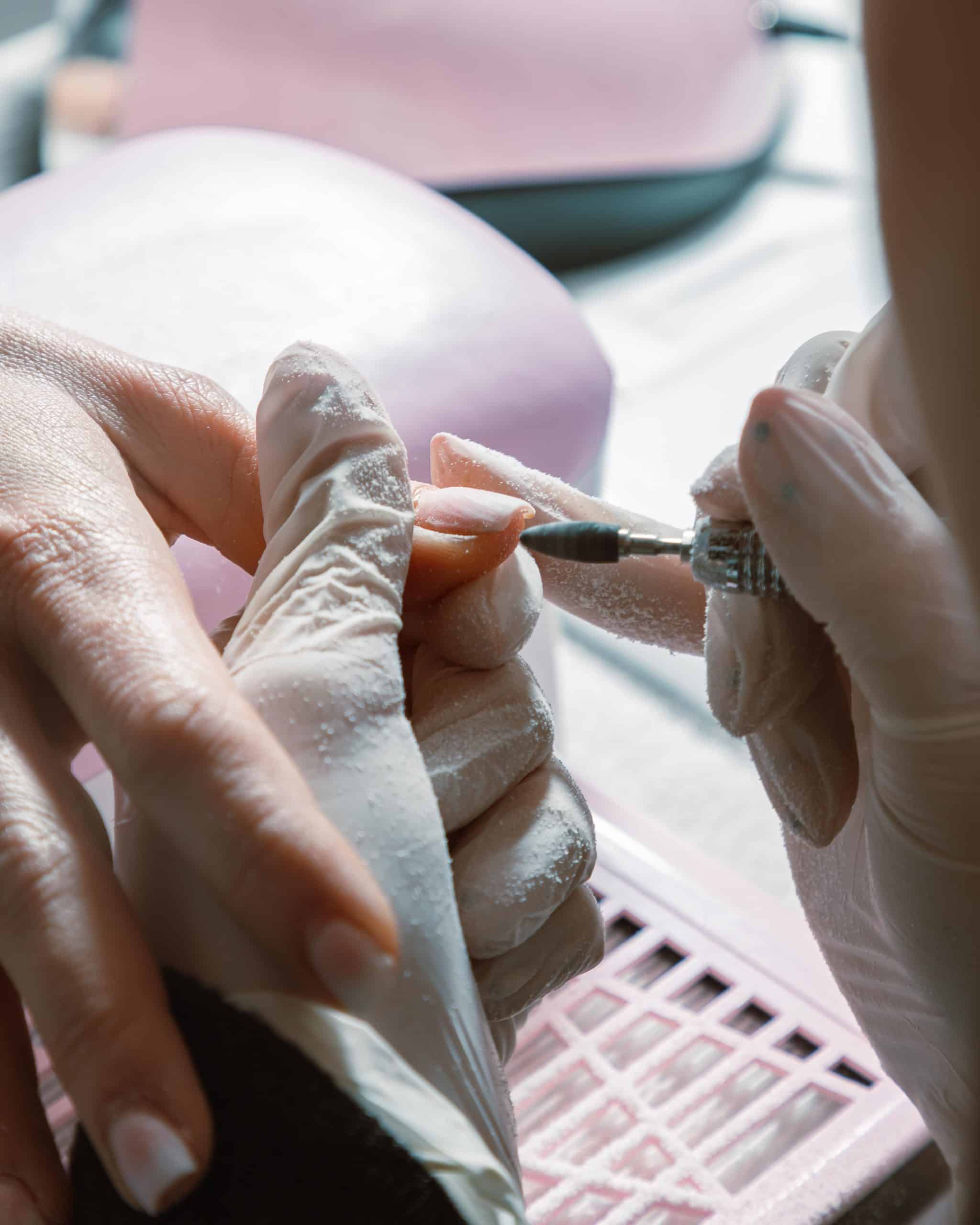Manicurist prepping and filing a nail before builder gel application