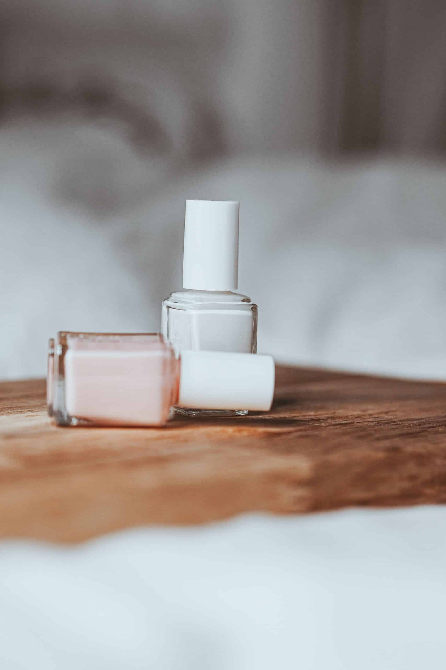 Two small labeled bottles of nail prep liquid standing side by side on a wooden tray