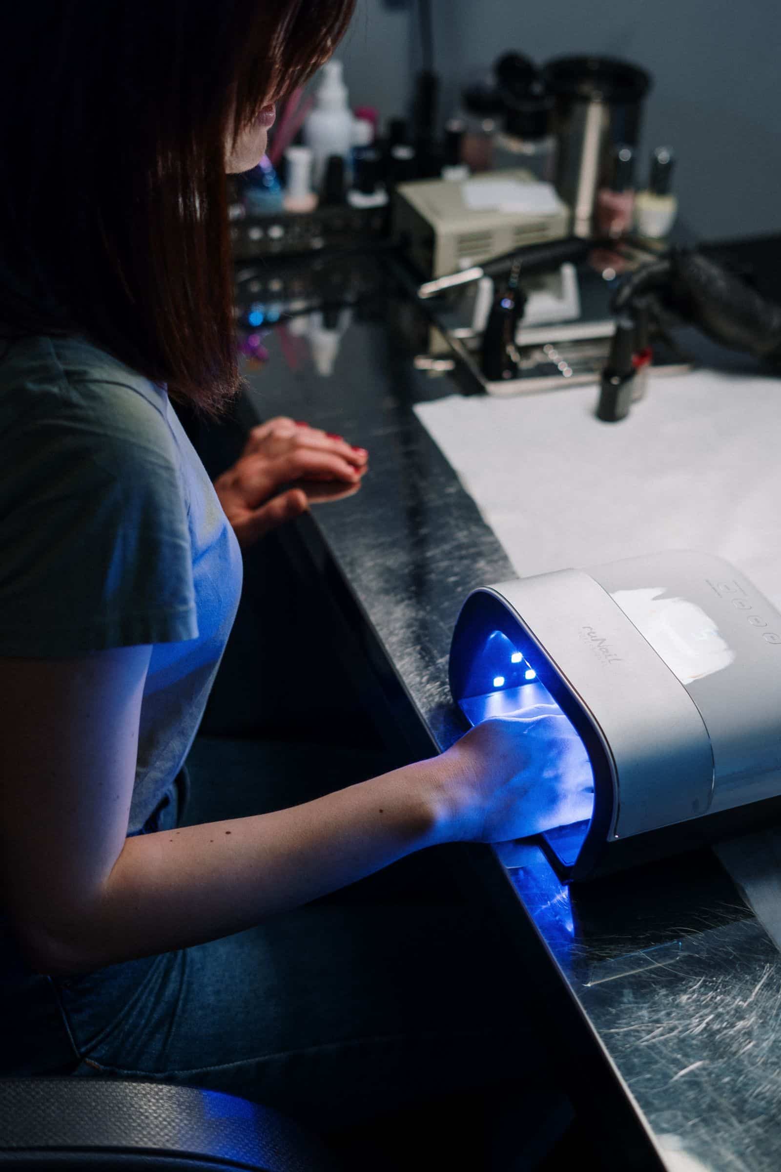 Client's hand curing under a UV nail lamp at a salon