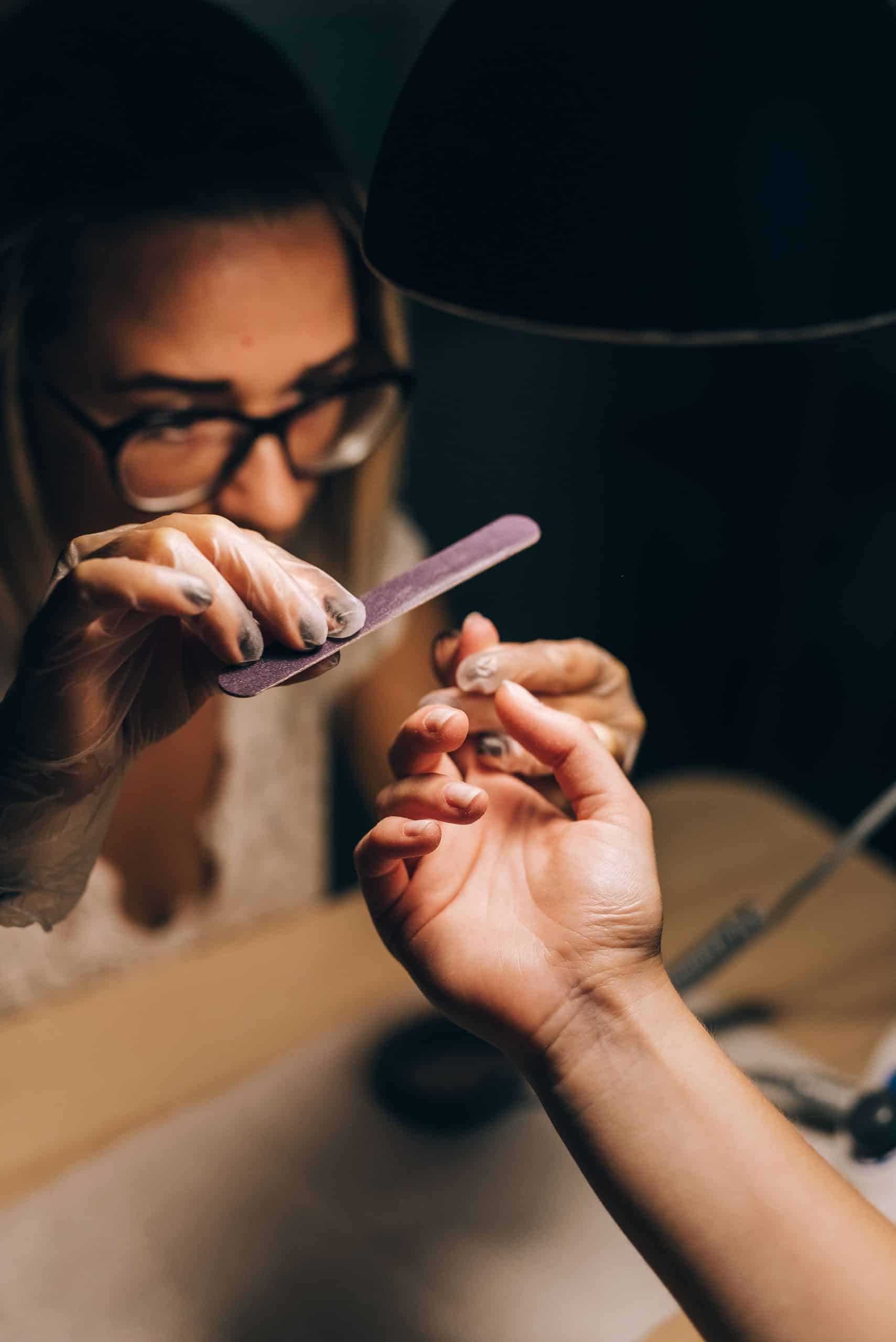 Close-up of a nail technician lightly buffing a client's nail plate during prep