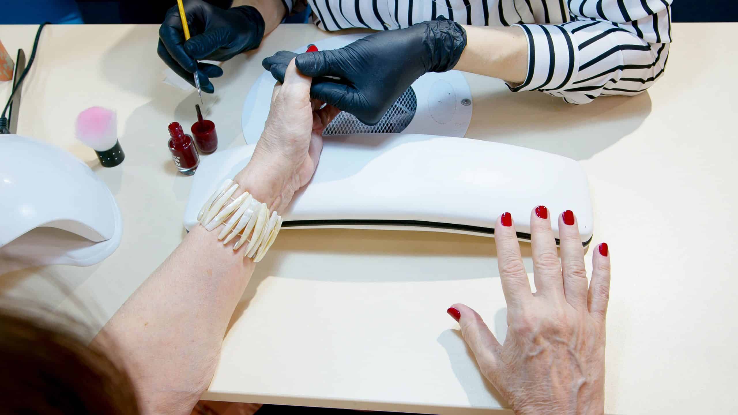 Manicurist applying red gel polish to a client's nail