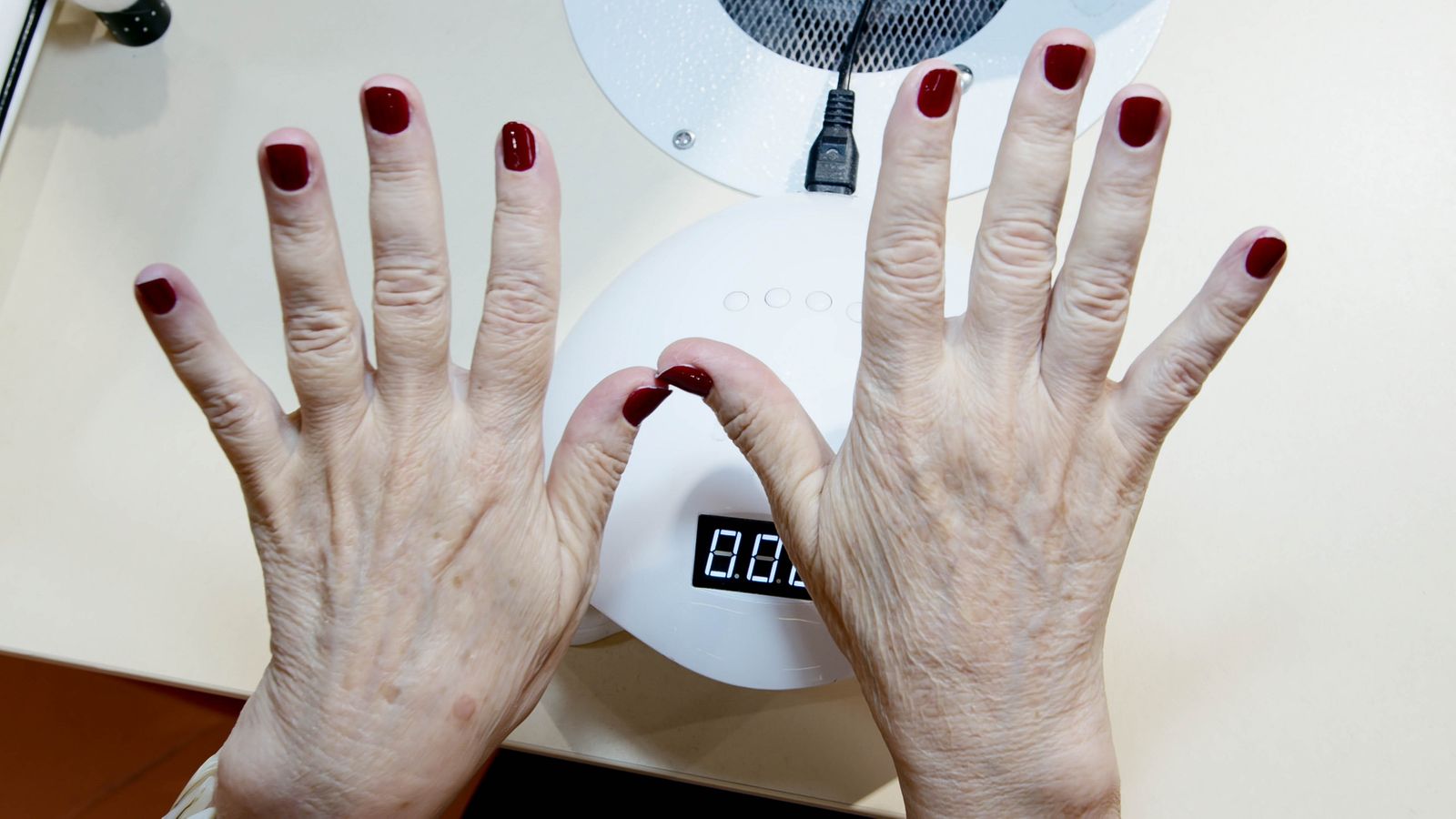 Hand with red nails curing under a nail drying lamp