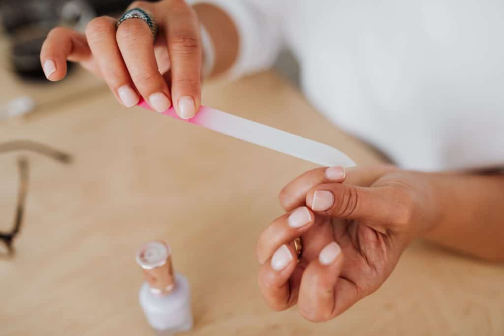 Close-up of hands filing a nail with a nail file next to a bottle of polish