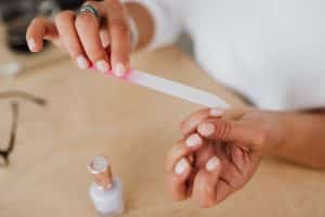 Close-up of hands filing a nail with a nail file next to a bottle of polish