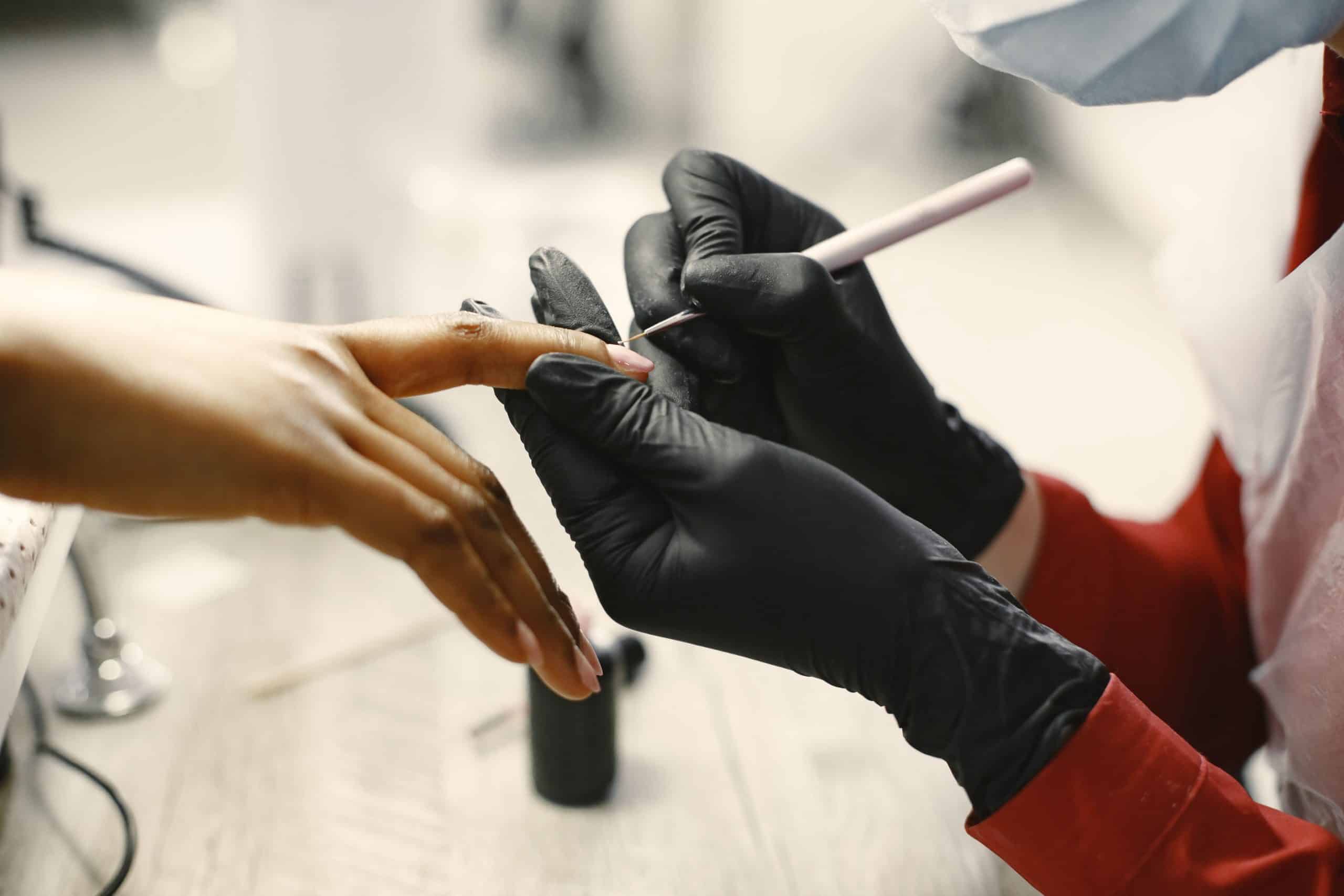 Nail technician's gloved hands with manicure tools on a salon table