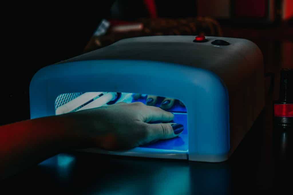 Hand with builder gel manicure curing under a UV LED nail lamp during a salon appointment
