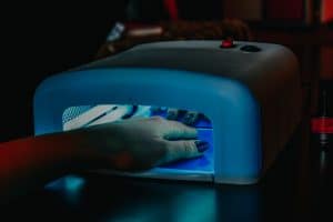 Hand with builder gel manicure curing under a UV LED nail lamp during a salon appointment