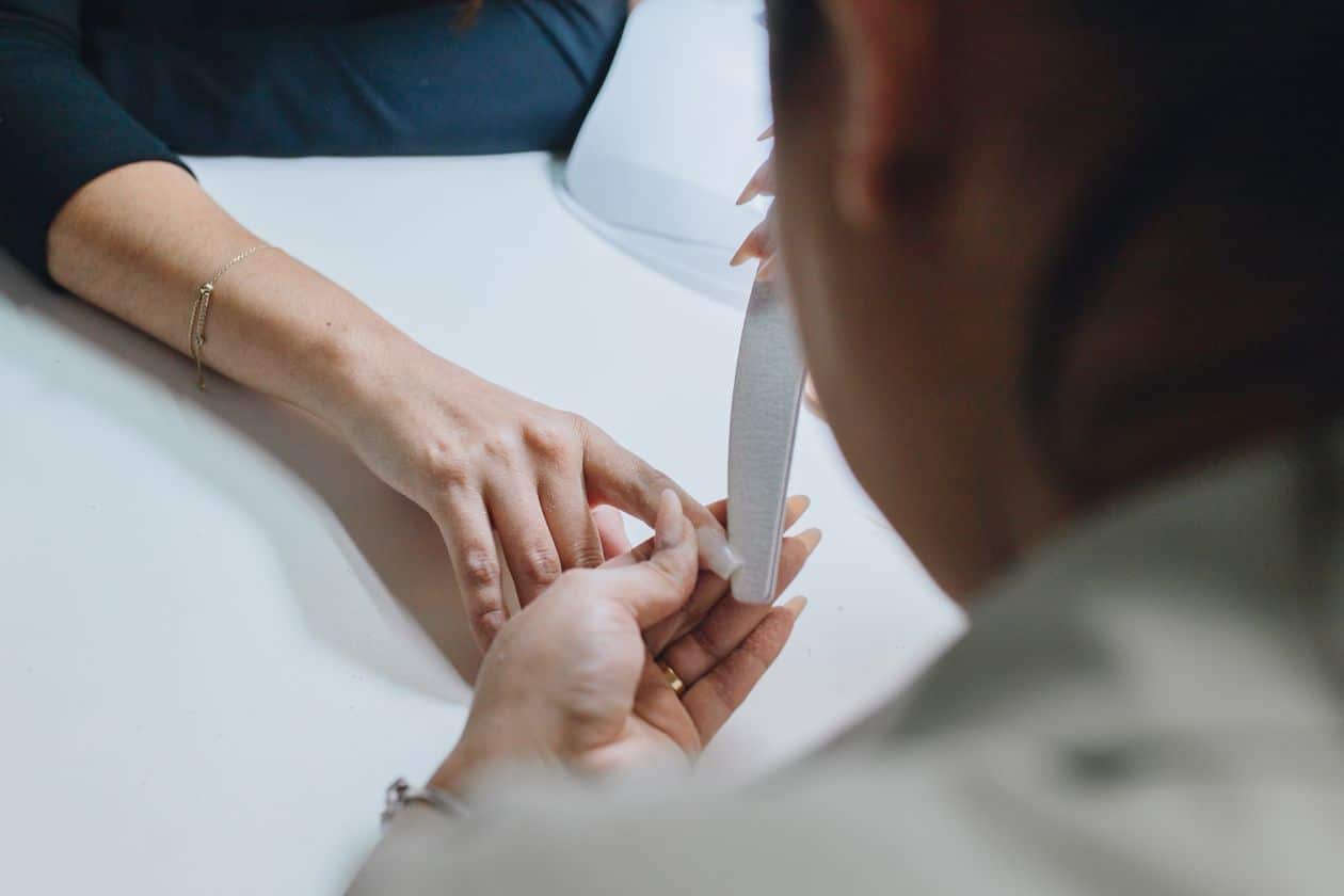 Close-up of a nail technician filing the regrowth area of an acrylic nail before a fill